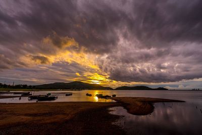 Scenic view of lake against dramatic sky during sunset