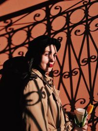 Portrait of woman holding drink standing against wall