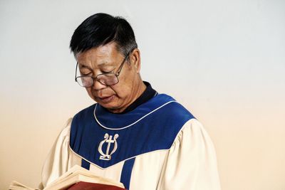 Close-up of priest reading book against colored background