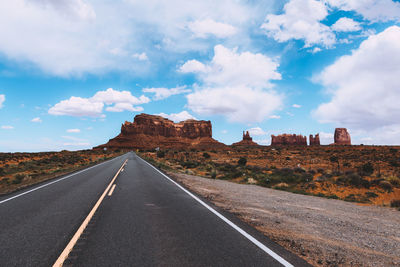 Road leading towards rock formations against sky
