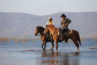 Men riding horses in lake against sky