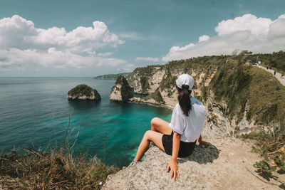 Woman sitting on shore by sea against sky