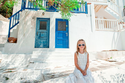 Portrait of young woman wearing sunglasses while standing against building