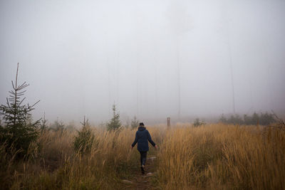 Rear view of woman walking at forest during foggy weather