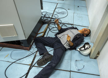 Shocked man holding cables while lying on floor by fuse box