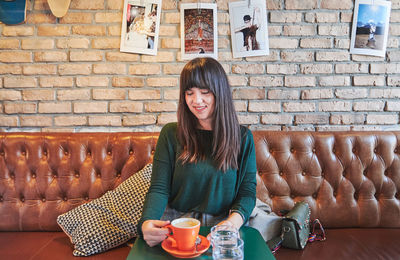 Portrait of young woman standing against wall at cafe