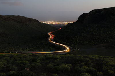 Light trails on road by mountain against sky at night