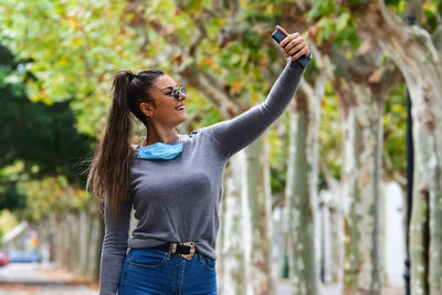 Young woman photographing while standing on tree