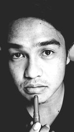 Close-up portrait of young man holding lipstick in darkroom