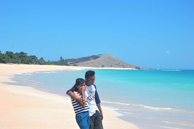 Young couple standing at beach against clear blue sky