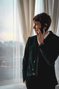 Young man using smart phone while standing on window