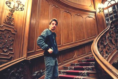 Portrait of young man standing on staircase against wall