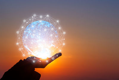 Person holding illuminated fireworks against sky during sunset