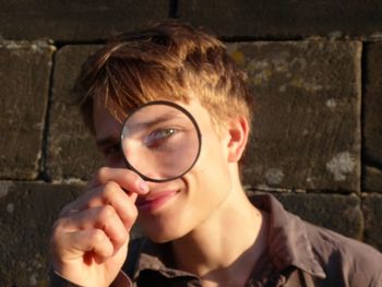 Close-up portrait of young woman holding eyeglasses against wall