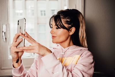 Woman using mobile phone while sitting against window