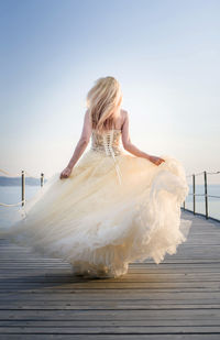 Rear view of bride walking on pier against sky