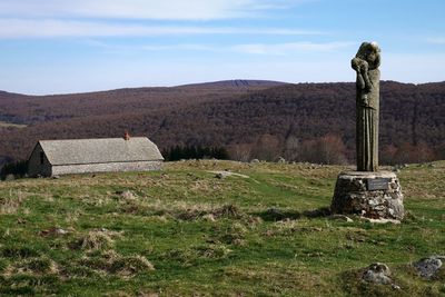 Old statue on field by mountain against sky