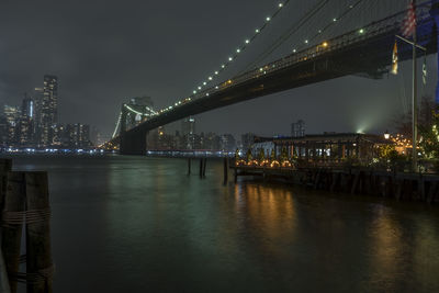 Illuminated bridge over river in city against sky at night