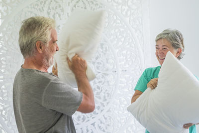 Cheerful senior couple having pillow fight at home