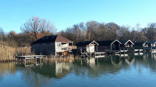 Houses by lake against buildings against clear blue sky