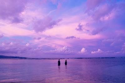 Silhouette couple standing in sea against purple sky during sunset