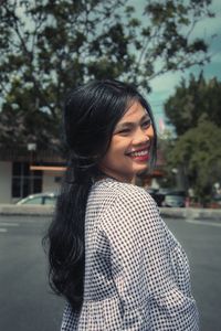 Portrait of smiling young woman standing against trees