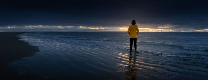 Rear view of woman standing on beach during sunset