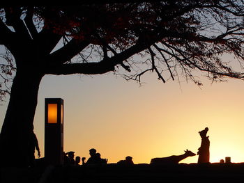 Silhouette people standing by tree against orange sky