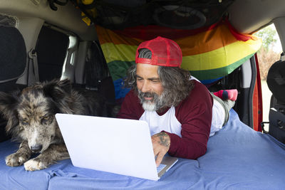 Man lying in the camping van with his pet and using a laptop.  remote computer working online 