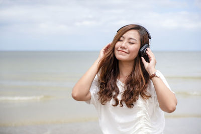 Smiling woman listening to music while standing at beach