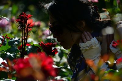 Side view of mature woman smelling red flowers in garden