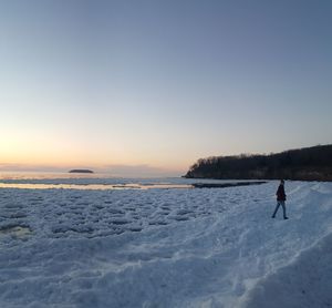 Mid distance view of person standing on snow covered field against sky