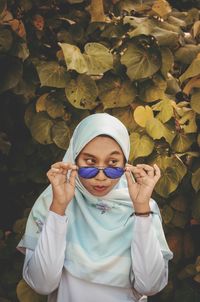 Young woman in hijab wearing sunglasses against leaves