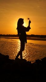 Silhouette girl standing hold dried flower on beach against sky during sunset