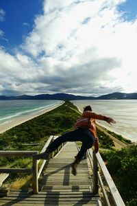 Playful man jumping on steps against sea