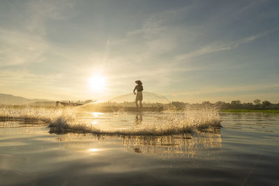 Man on lake against sky during sunset