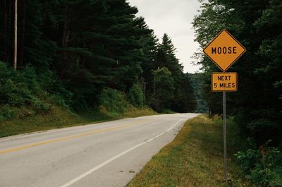 Road sign by trees against sky