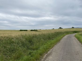 Empty road amidst field against sky