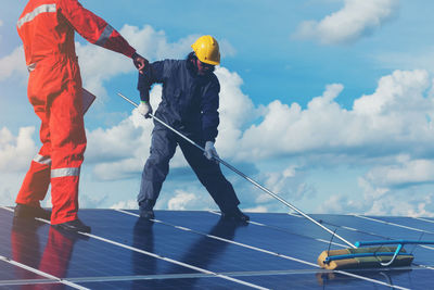 Low angle view of male technicians working on solar panels against sky