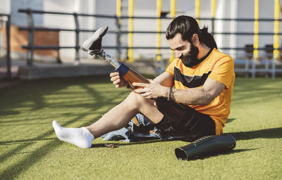 Smiling athlete wearing prosthetic leg sitting on grass