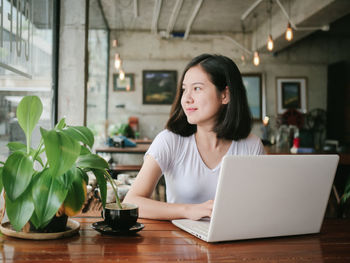 Smiling young businesswoman using laptop on table at cafe