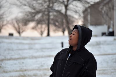 Man in hooded jacket and looking away while standing on snow covered field