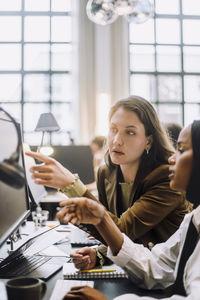 Mid adult businesswoman discussing over desktop pc with female colleague in office