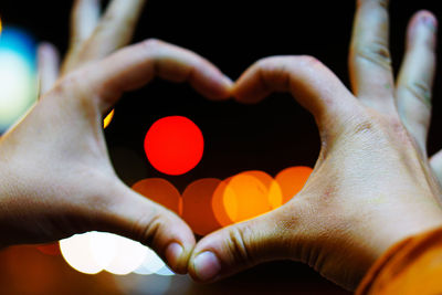 Cropped hands of people making heart shape over defocused lights at night