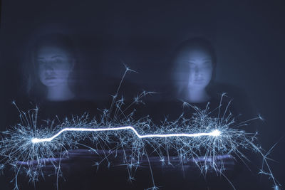 Multiple image of woman holding illuminated sparklers at night