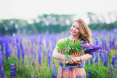 Young attractive woman holding a basket full of lupine flowers