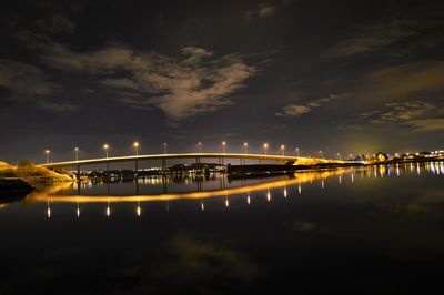Illuminated bridge over river against sky at night