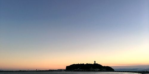 Silhouette built structure by sea against clear sky