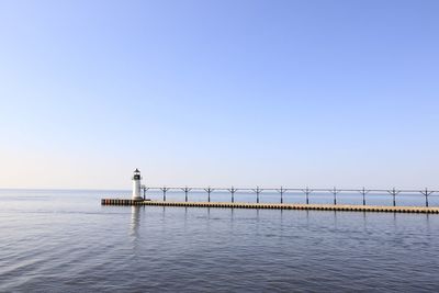 Lighthouse on pier over sea against clear sky