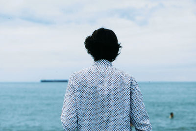 Rear view of man standing at beach against sky